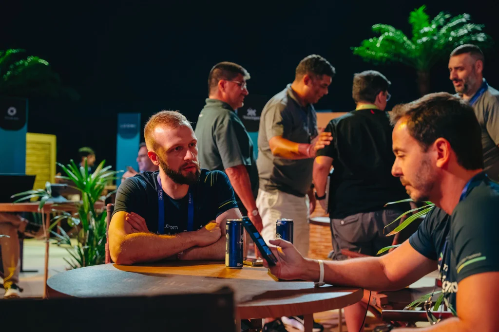 Dois executivos conversando em uma mesa durante o evento IT Forum Praia do Forte 2026, com iluminação quente e palmeiras ao fundo.